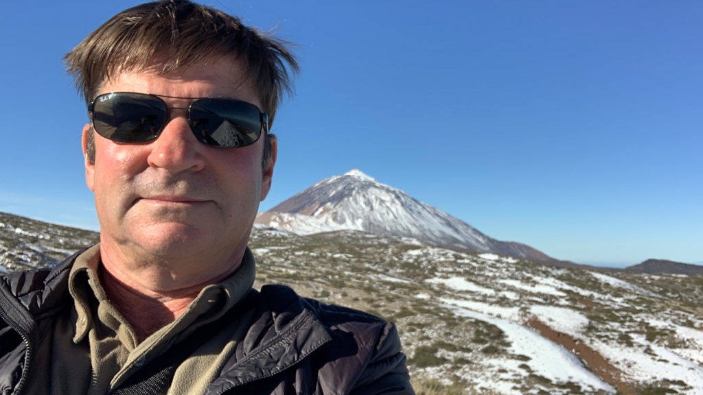 Selfie eines Mann mit dunkler Sonnenbrille. Im Hintergrund sieht man den Teide mit Schnee