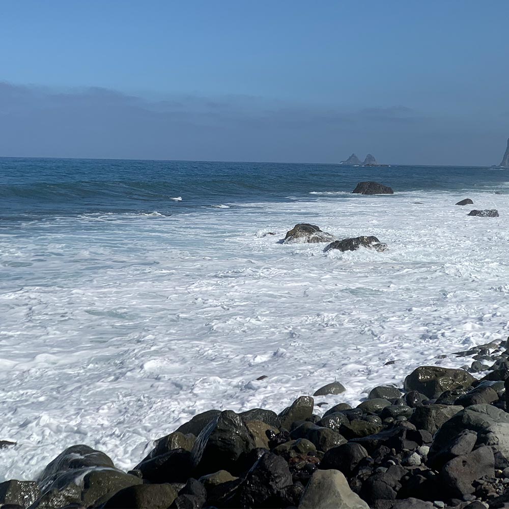 Der Küstenabschnitt El Cardonal mit großen Lavasteinen, Meereswellen und der Felsformation Las Baja im Hintergrund
