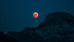 Ein rötlicher Vollmond bei Mondfinsternis hinter einem dunklen Bergrücken