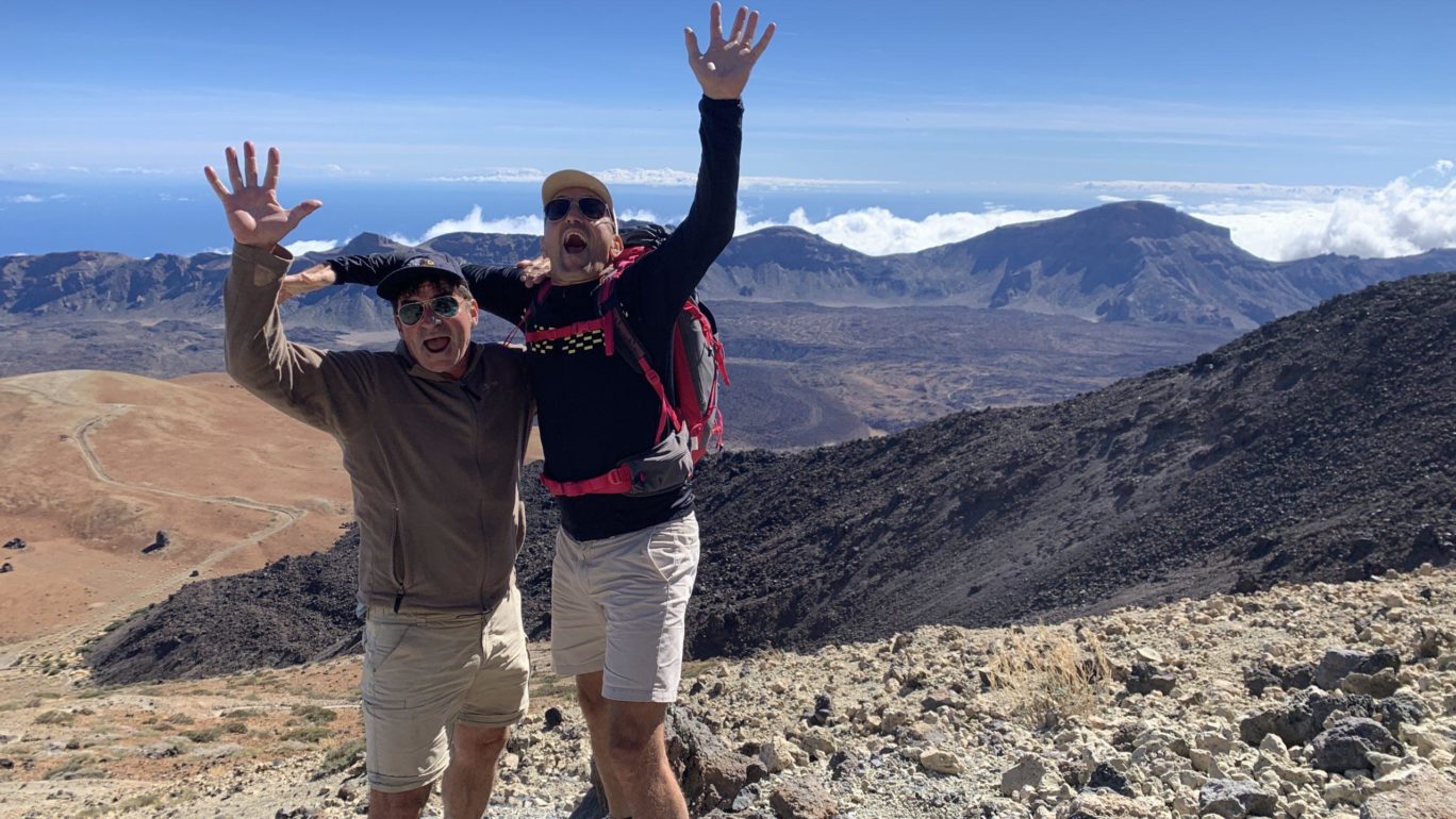Zwei Männer springen vor Begeisterung mit erhobenen Händen in die Luft. Im Hintergrund die Caldera am Pico del Teide