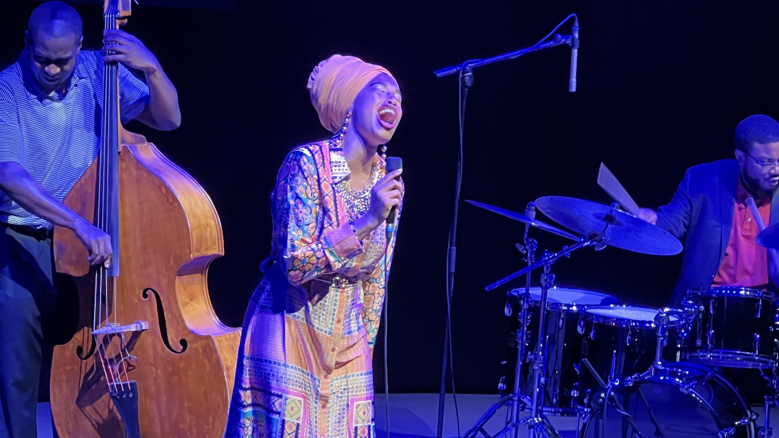 Jazzsängerin Jazzmeia Horn in buntem Kleid und Turban singt sehr emotional ein Lied.